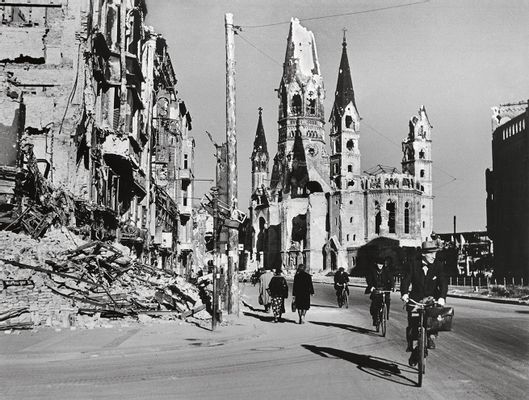 Robert Capa - Les gens le long d'une rue bordée de bâtiments détruits